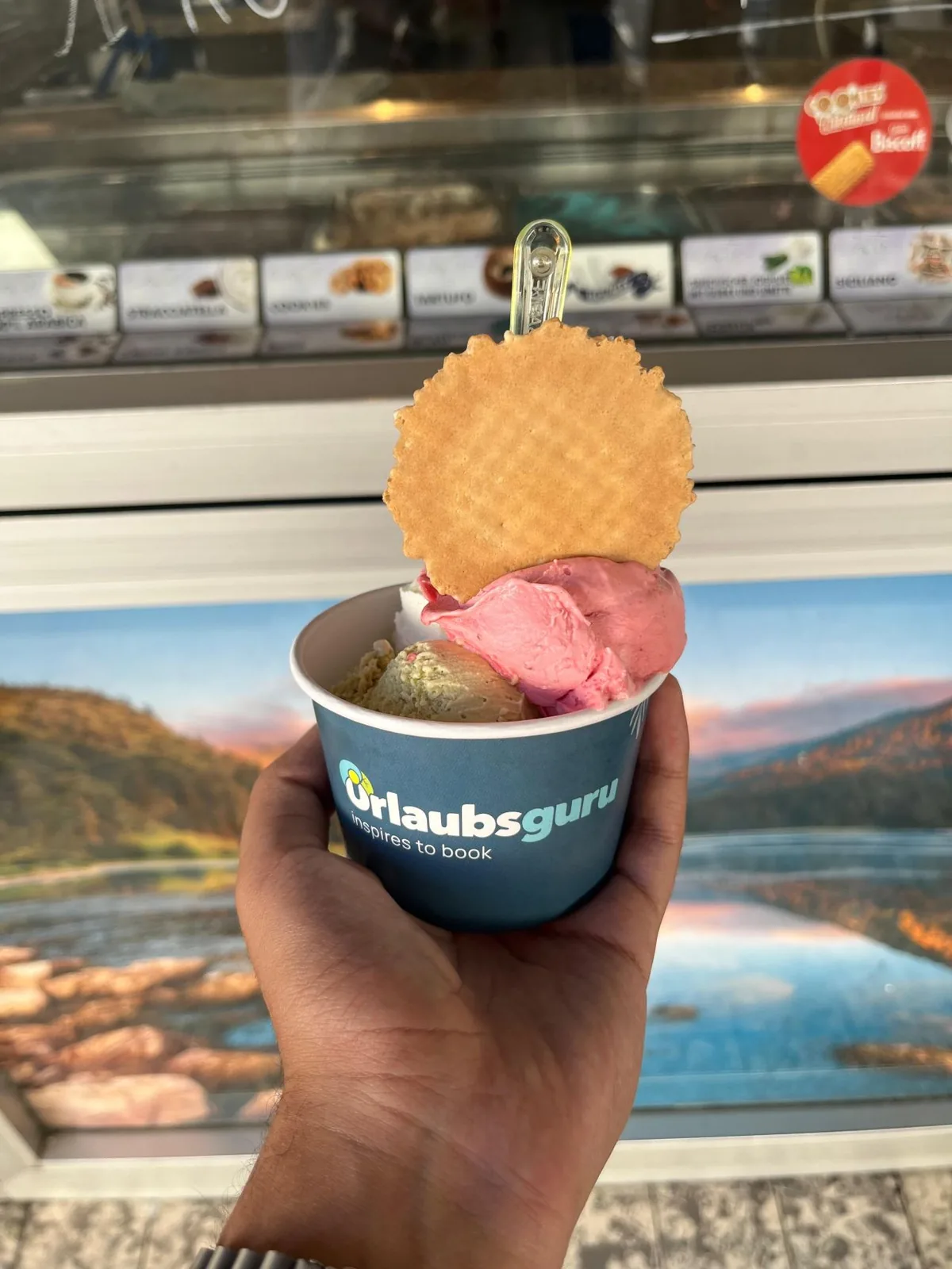 Hand hält einen bedruckten Eisbecher mit Eis und Waffel