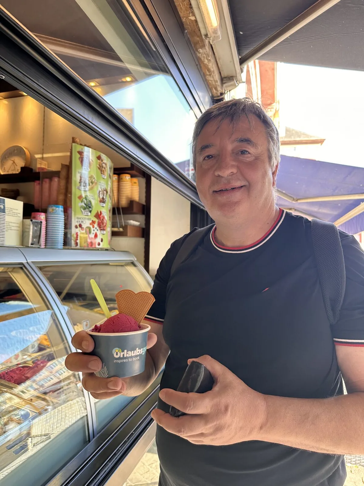 Gast mit bedrucktem Urlaubsguru-Eisbecher vor der Eistheke