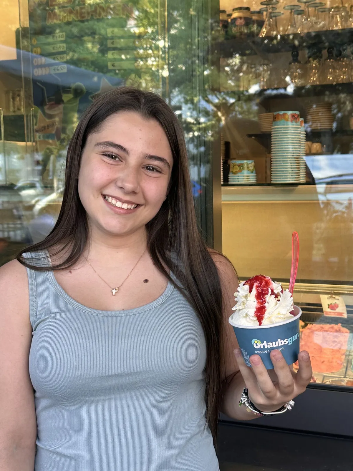 Promoterin hält einen bedruckten Urlaubsguru-Eisbecher vor der Eisvitrine