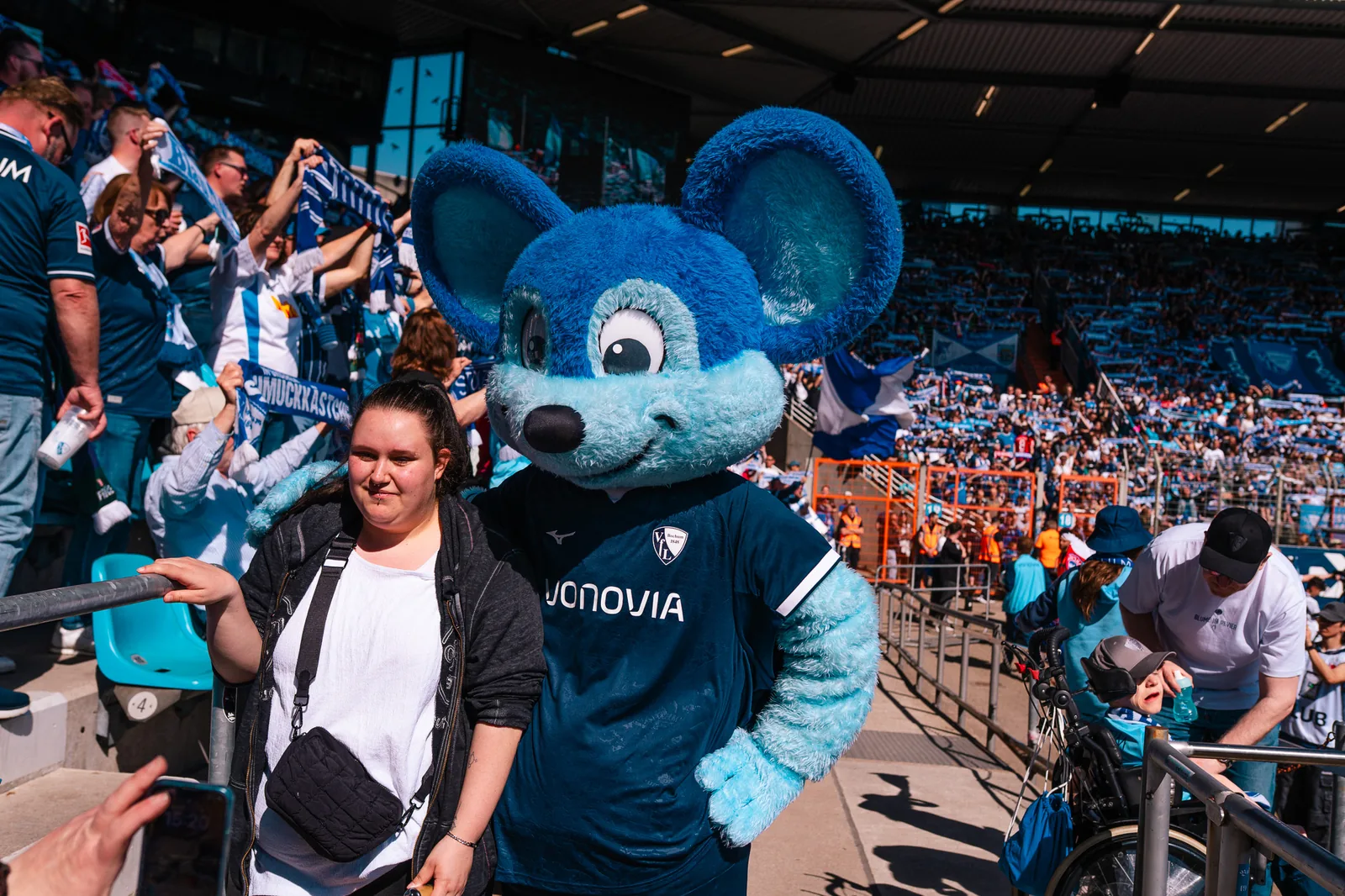 Promoterin verteilt Give-aways im Stadion neben dem Vereinsmaskottchen