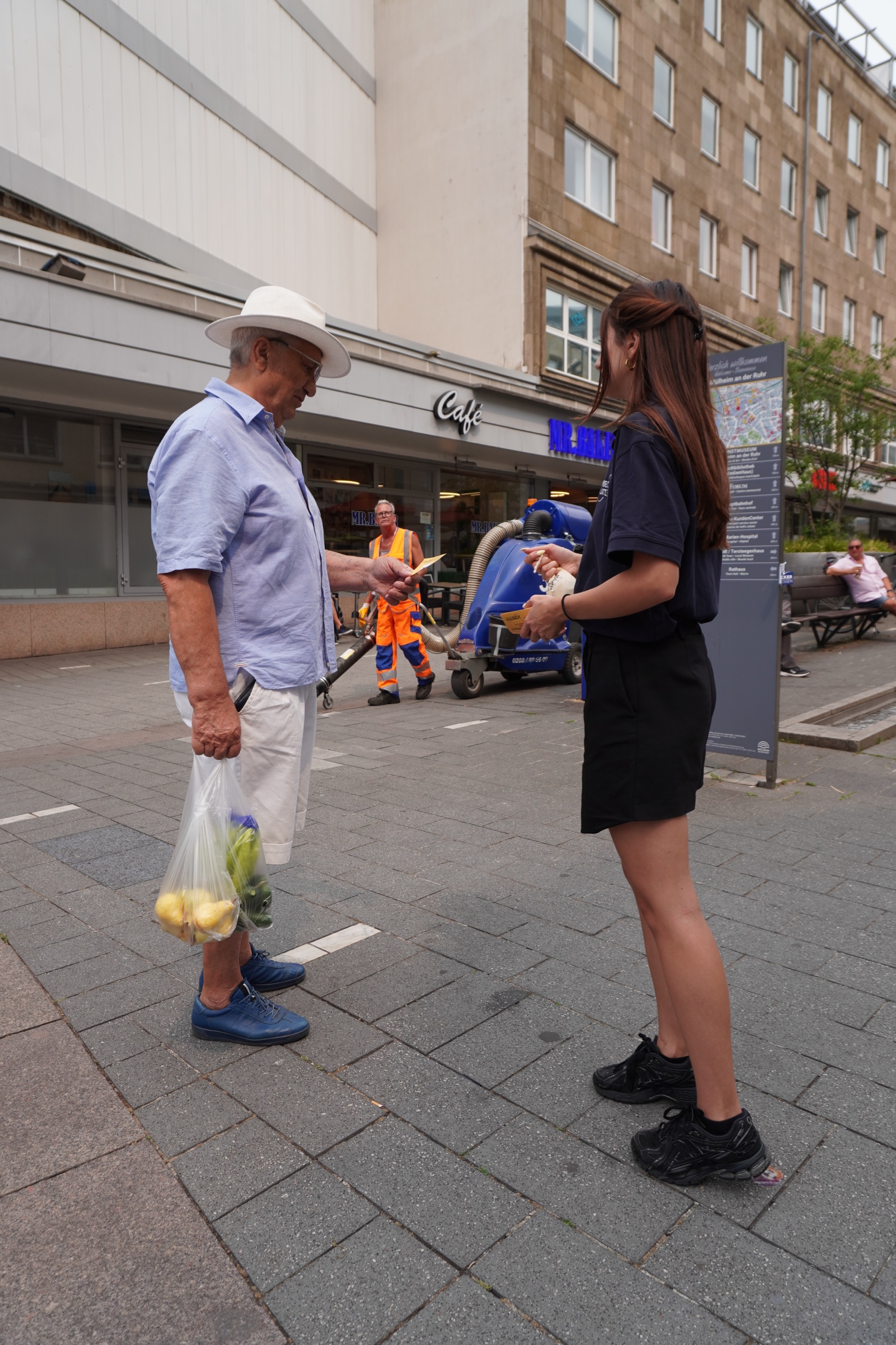 Promoterin uebergibt einem Passanten einen 5-Euro-Gutschein in der Fussgaengerzone