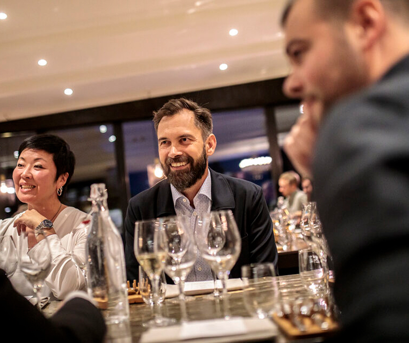Three people smiling and talking around a table at a work dinner in a warmly lit restaurant.