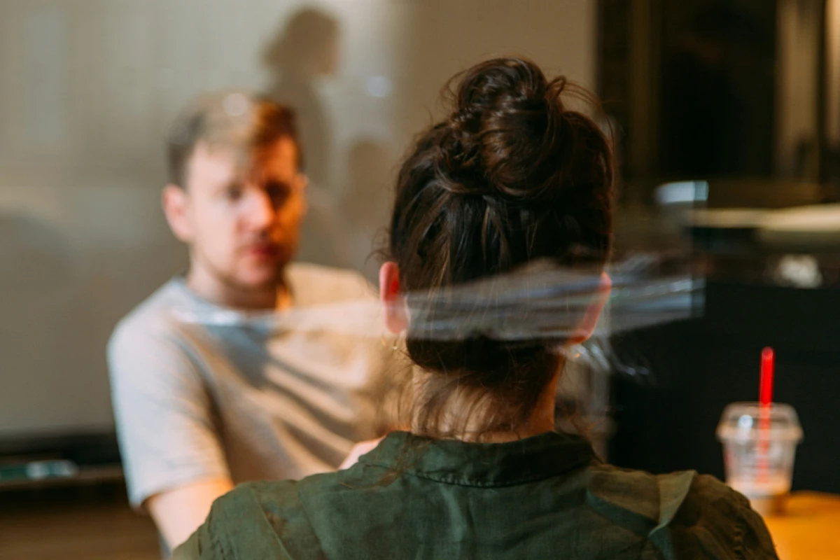 Two people having a conversation inside of a glass-walled conference room.