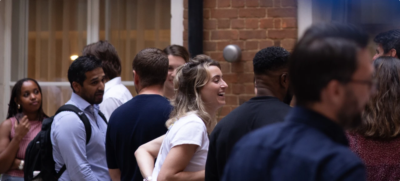 A diverse group of people socialising indoors, with one woman laughing and others engaged in conversation.