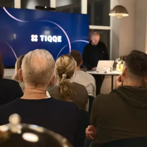 A TIQQE speaking event with a person presenting in front of a crowd