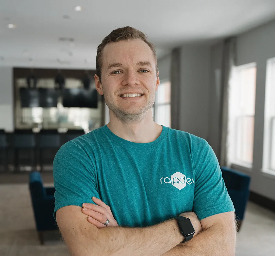 Smiling man in a teal shirt stands confidently with arms crossed.