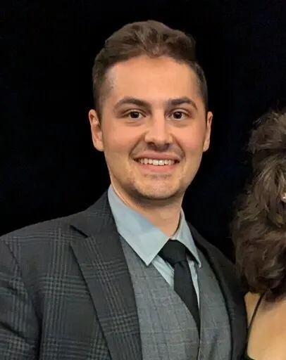 Smiling man in a suit with a light blue shirt and tie.