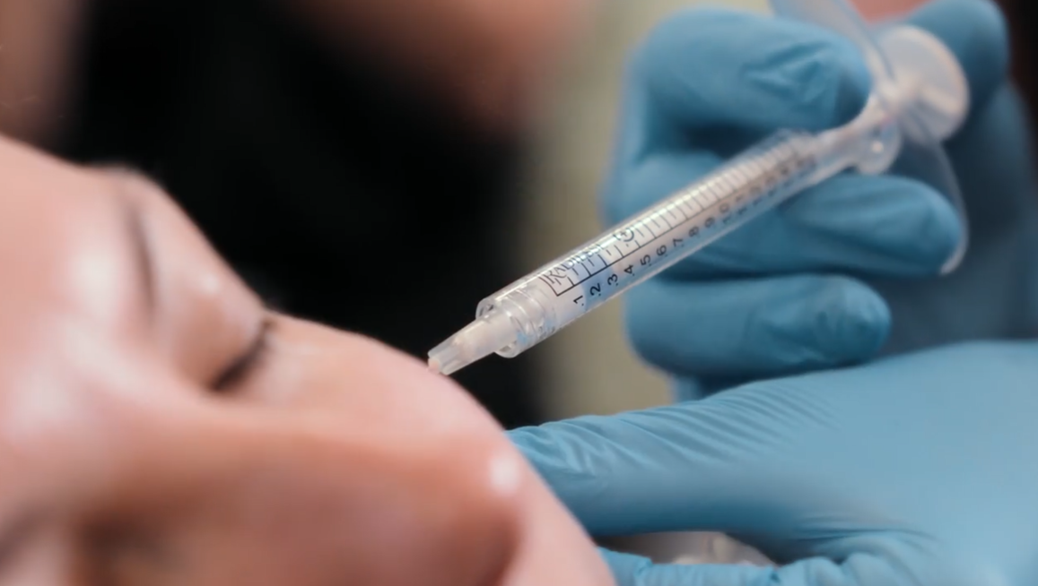 Close-up of a gloved hand administering a nasal injection with a syringe to a person's nose.