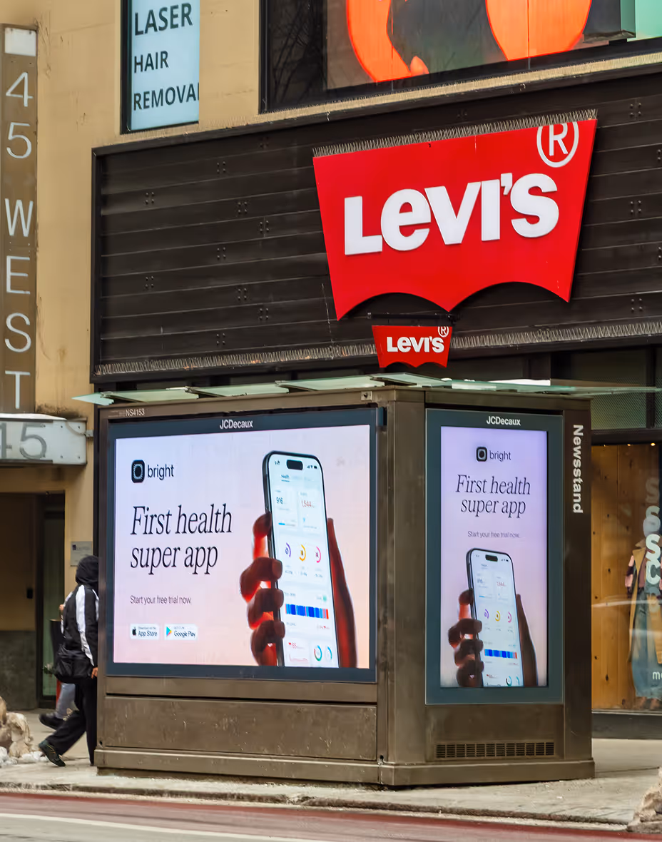 Street corner newsstand with digital ads for the Bright health app and a large Levi's store sign above.