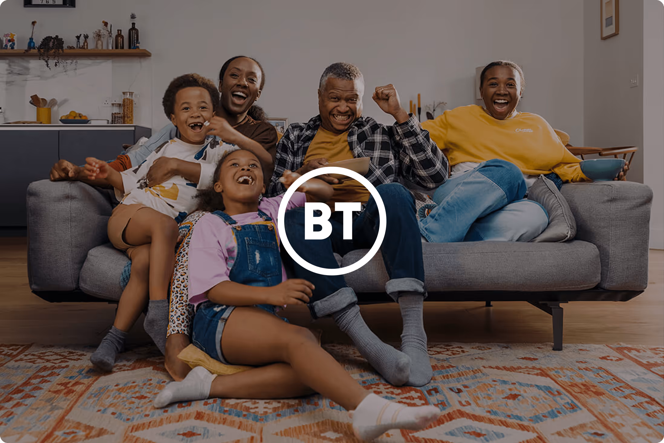 The BT logo atop brand imagery from BT showing a family piled onto a sofa watching television