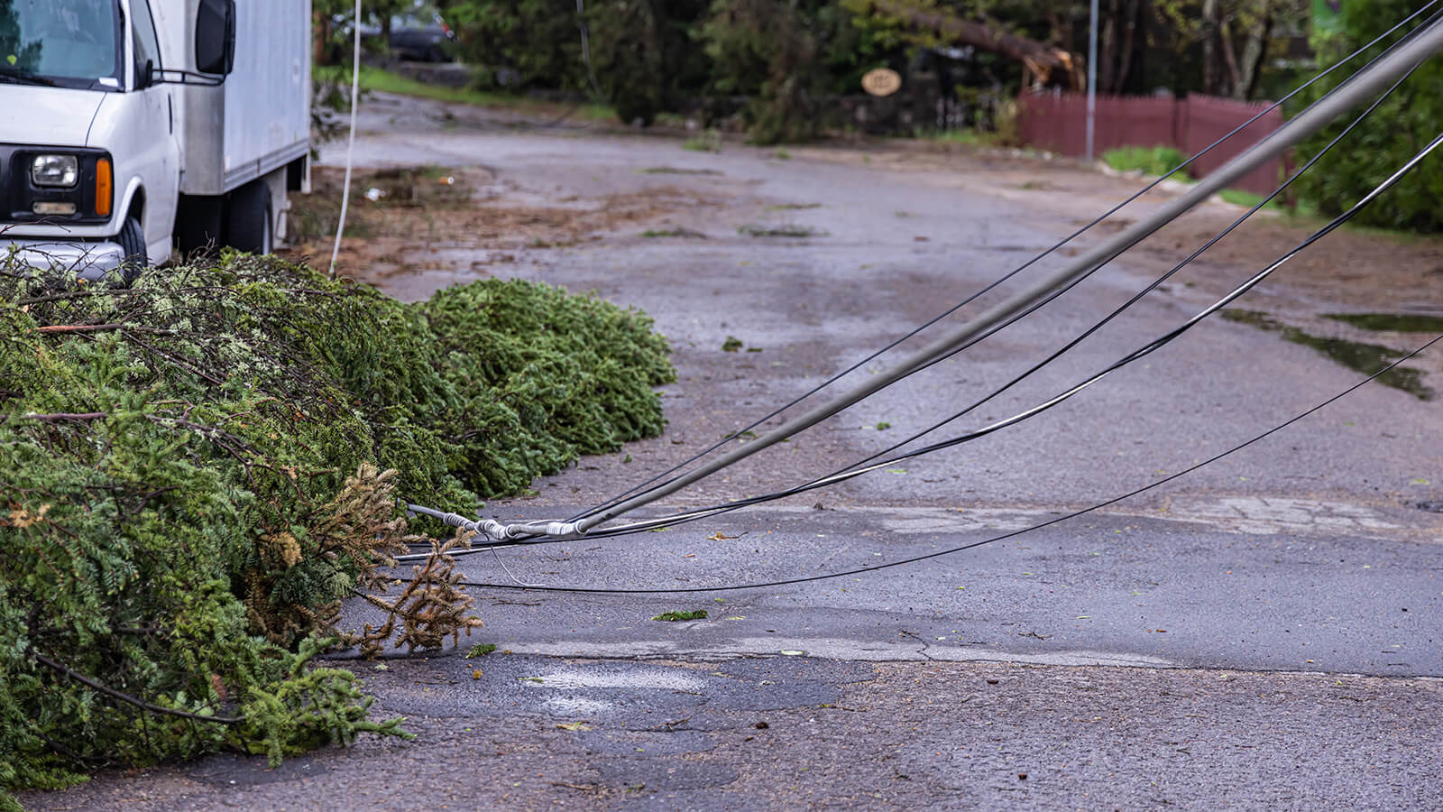 Downed utility lines and storm debris blocking a wet roadway after damaging winds.