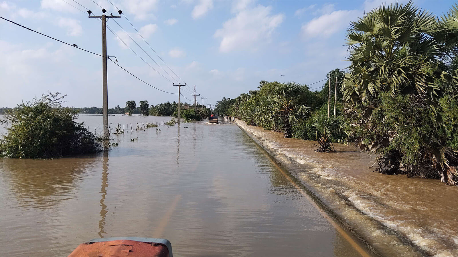 Floodwater covering a roadway lined with utility poles after severe weather.