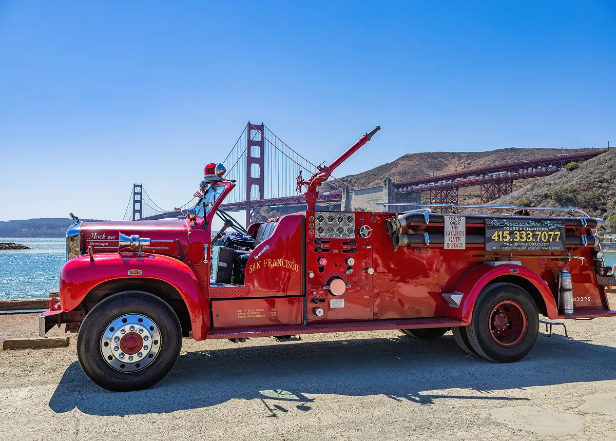 Vintage red San Francisco fire truck parked near the Golden Gate Bridge on a sunny day.