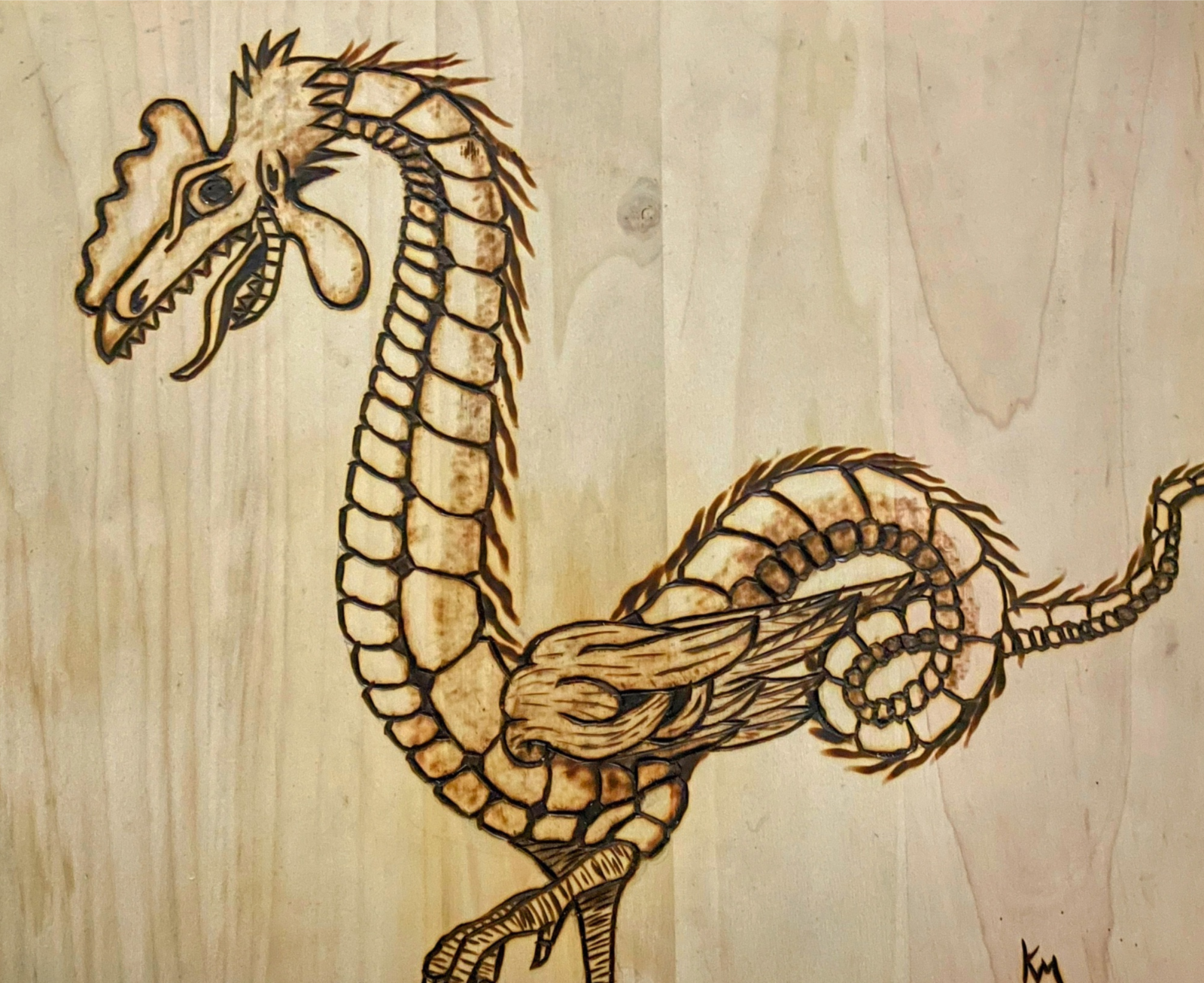 Woodburned abstract dragon with segmented body, wings, and detailed head on light wooden background.