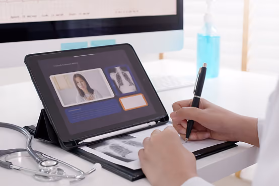 Doctor reviewing chest X-rays on a tablet and writing notes at a desk with a stethoscope nearby.