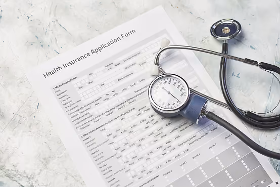 Health insurance application form on a marble surface with a stethoscope and blood pressure monitor.