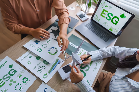Two people working on ESG sustainability reports with charts and a small wind turbine model.
