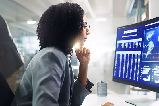 Woman with curly hair and glasses analyzing stock market data on a computer screen.