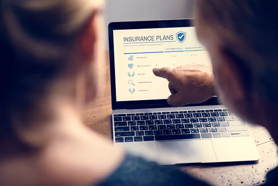 Two people looking at insurance plans on a laptop screen with a finger pointing to details.