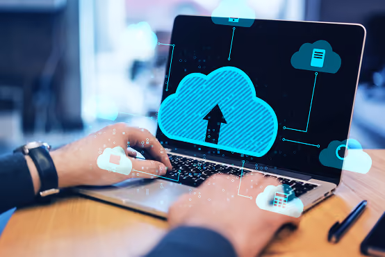 Person using laptop with digital cloud upload icons floating over the screen.