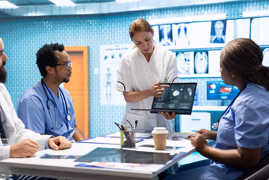 Medical team reviewing brain scan images on a tablet during a meeting in a hospital room.