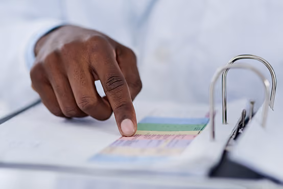 Person pointing at color-coded document inside a white binder with metal rings.