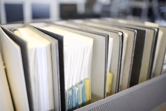 Close-up of black binders with paper and colored tabs standing in an office filing shelf.