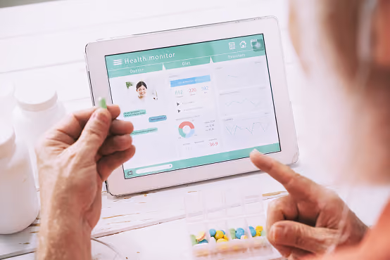 Person holding a pill near a tablet displaying health monitor data and a weekly pill organizer.