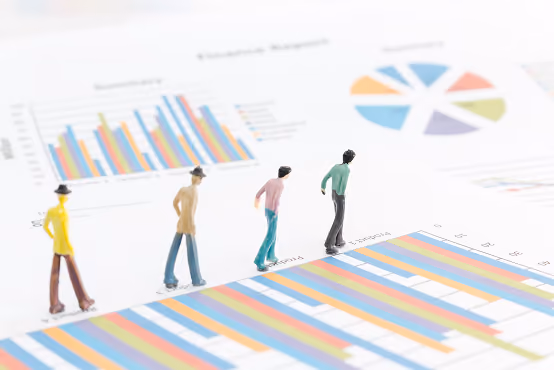 Miniature figures standing on printed multicolored bar and pie charts representing data analysis.
