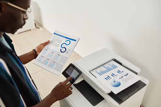 Person using a printer with printed charts and graphs on paper placed in the output tray.