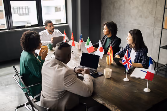 Diverse group having a meeting around a table with laptops and small international flags.