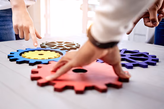Two people assembling colorful interlocking gears on a table in a collaborative setting.
