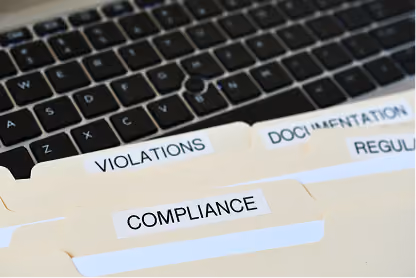 File folders labeled Compliance, Violations, Documentation, and Regulations on a laptop keyboard.