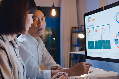 Two professionals discussing business data shown on a computer screen in an office setting.
