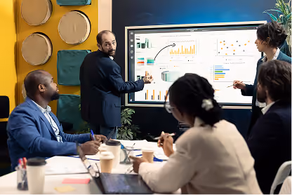 Business team discussing charts and data on a large screen in a modern office meeting.