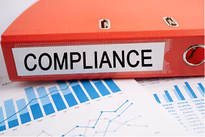 Red binder labeled compliance placed on documents with business charts and graphs.