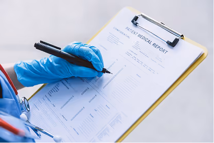 Medical professional wearing blue gloves writing on a patient medical report on a clipboard.
