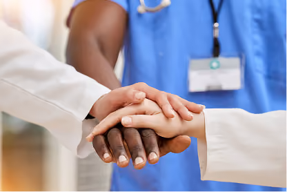 Three healthcare professionals stacking hands symbolizing teamwork and support.