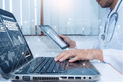 Doctor using a laptop and holding a tablet with medical data visuals and network connections overlaid.