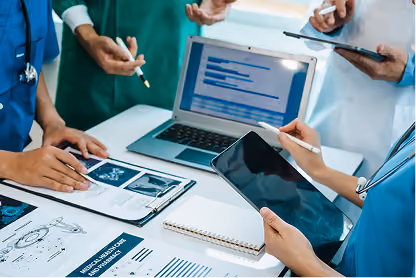 Medical professionals reviewing charts, x-rays, and patient data on a tablet and laptop at a desk.