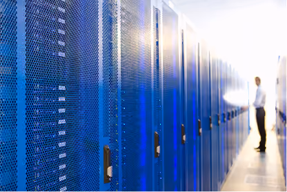 Man standing in a corridor between rows of blue server racks in a data center.