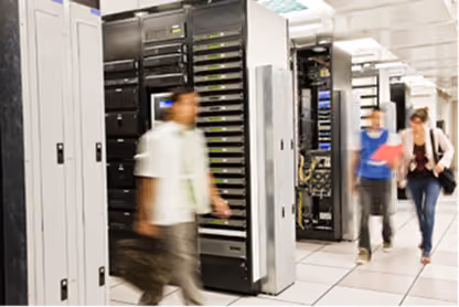 Blurred people walking in a server room with racks of computer servers and equipment.