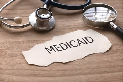 Stethoscope and magnifying glass beside torn paper with the word Medicaid on wooden surface.