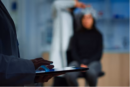 Doctor in white coat using tablet with patient in head scan cap in blurred background.