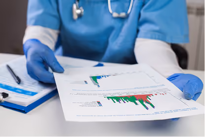 Person in blue scrubs and gloves holding a paper with bar charts and graphs.