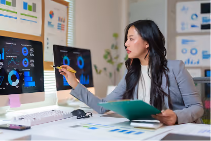 Businesswoman analyzing data and charts on computer screens in a modern office setting.