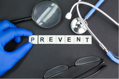 Gloved hand arranging letter tiles spelling PREVENT with stethoscope, magnifying glass, and glasses nearby.