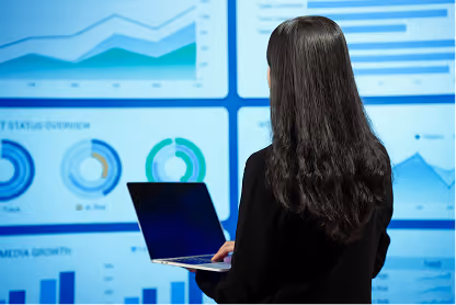 Woman with long black hair using laptop while looking at charts and graphs on a digital screen.