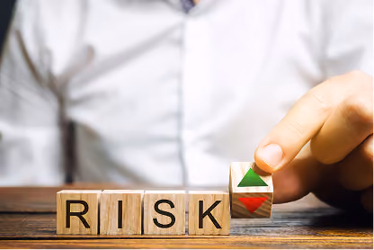 Hand flipping a block from red down arrow to green up arrow above wooden blocks spelling RISK.