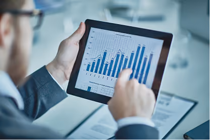 Person using a tablet showing a blue bar and line graph with data and charts in an office setting.